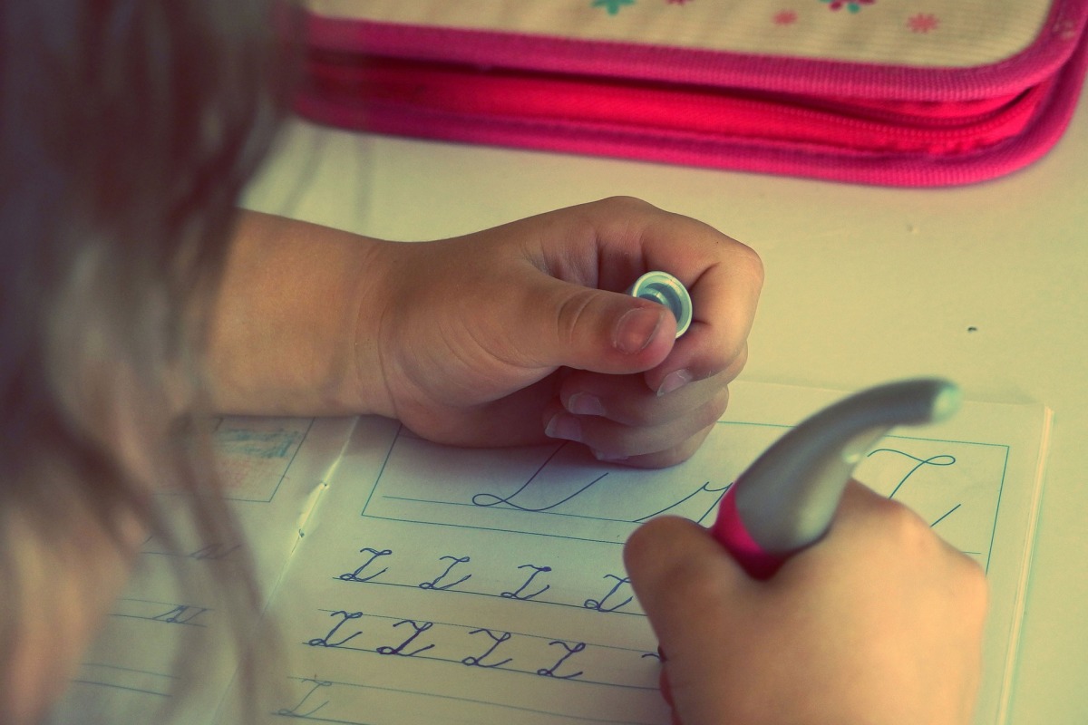 Zu sehen ist ein blondes Mädchen von hinten, das Schreiben übt. Sie hat einen pinken Stift in der Hand. Zu sehen ist ein blondes Mädchen von hinten, das Schreiben übt. Sie hat einen pinken Stift in der Hand.